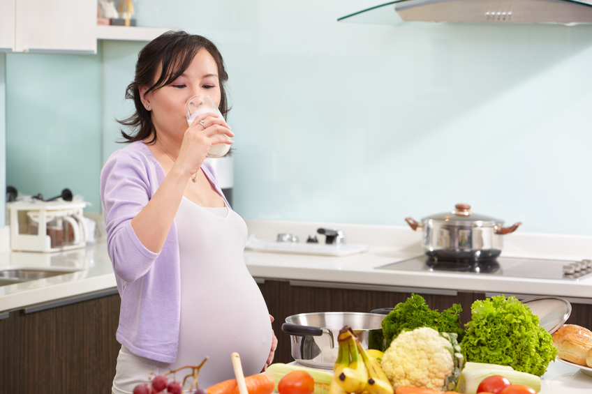 Chinese pregnant lady drinking milk in the kitchen